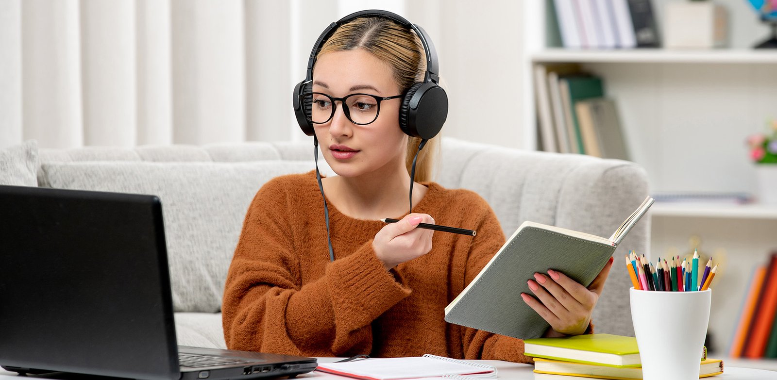student online cute girl in glasses and sweater studying on computer writing down notes
